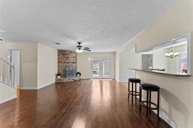 living room featuring wood walls, french doors, ceiling fan with notable chandelier, a fireplace, and dark hardwood / wood-style flooring