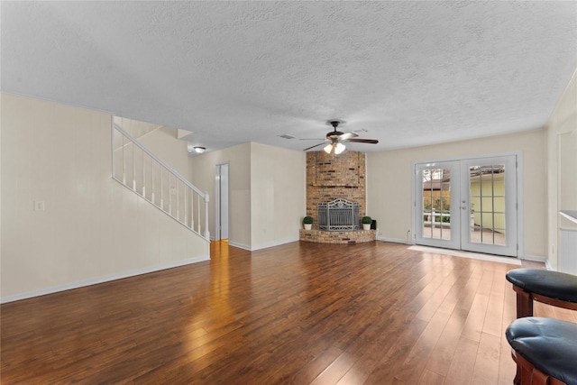 living room with french doors, a brick fireplace, hardwood / wood-style flooring, ceiling fan, and a textured ceiling