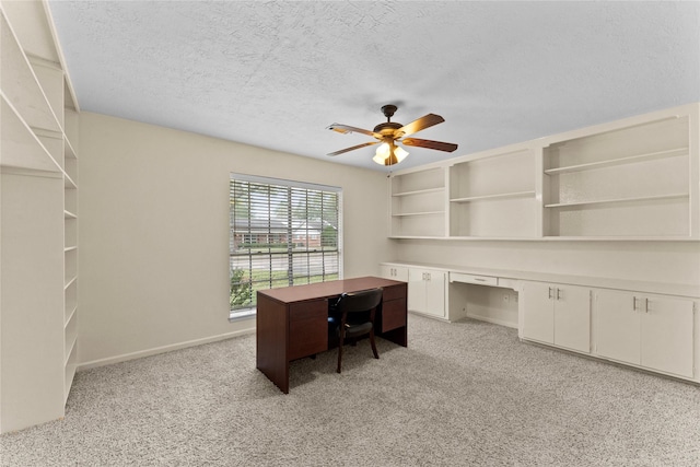 carpeted office space featuring ceiling fan, built in desk, and a textured ceiling