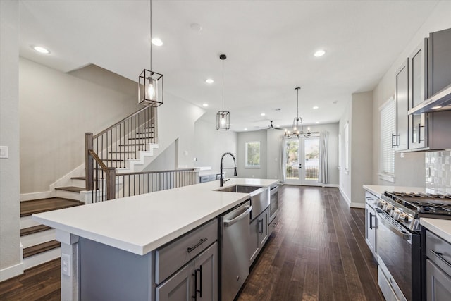 kitchen with hanging light fixtures, dark hardwood / wood-style floors, gray cabinets, a kitchen island with sink, and appliances with stainless steel finishes