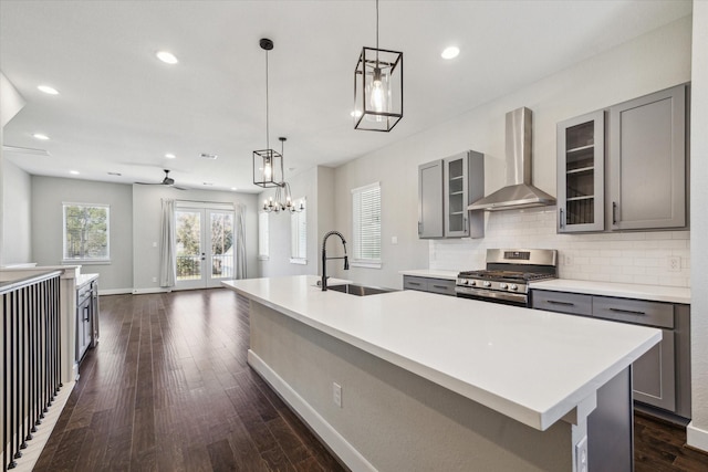 kitchen with gas stove, a kitchen island with sink, wall chimney exhaust hood, and sink