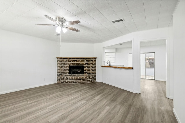 unfurnished living room featuring hardwood / wood-style floors, a brick fireplace, ceiling fan, and sink