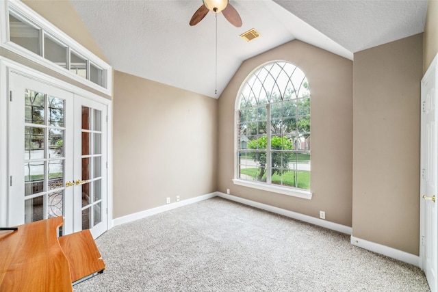 carpeted empty room featuring ceiling fan, vaulted ceiling, a textured ceiling, and french doors