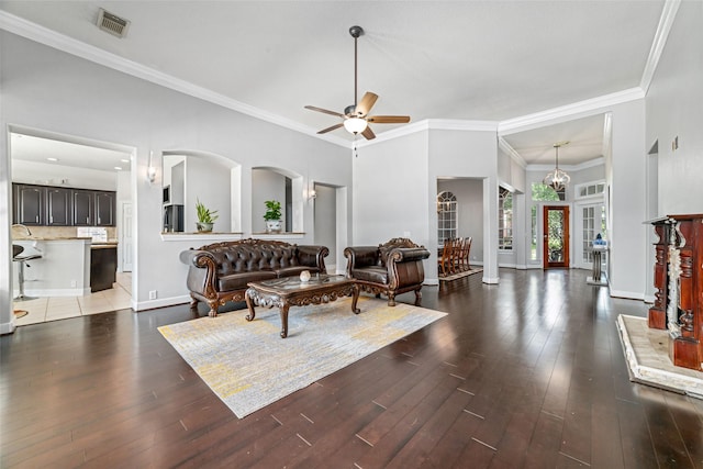 living room with ceiling fan with notable chandelier, dark wood-type flooring, and crown molding