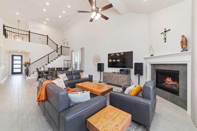 living room featuring ceiling fan, light wood-type flooring, a high ceiling, and a tile fireplace