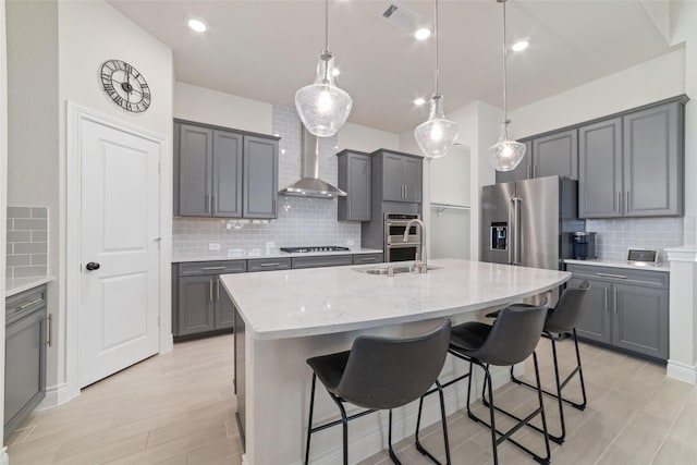 kitchen featuring pendant lighting, a kitchen island with sink, gray cabinetry, and wall chimney range hood