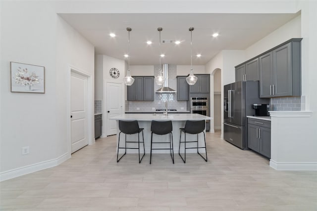 kitchen with gray cabinetry, a center island with sink, decorative backsplash, appliances with stainless steel finishes, and decorative light fixtures