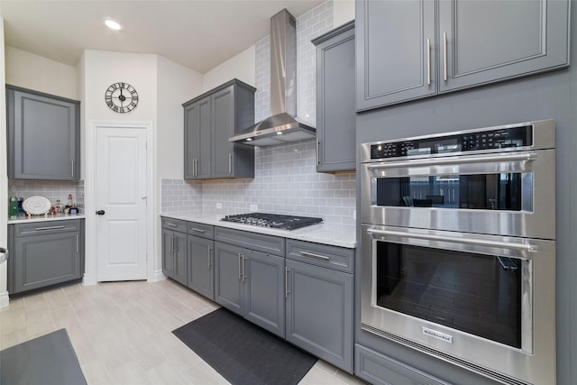 kitchen with decorative backsplash, appliances with stainless steel finishes, gray cabinets, and wall chimney exhaust hood