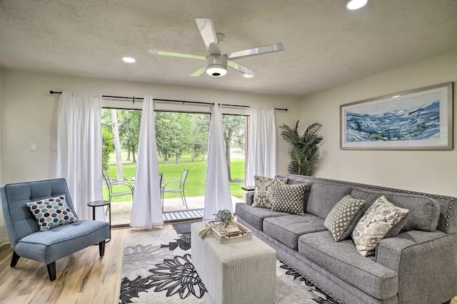 living room featuring ceiling fan, a textured ceiling, and light wood-type flooring