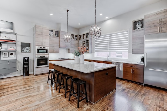 kitchen featuring hardwood / wood-style floors, sink, a kitchen island, light stone counters, and stainless steel appliances