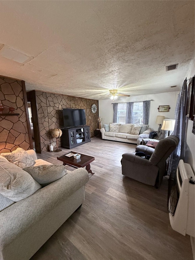 living room with heating unit, ceiling fan, hardwood / wood-style floors, and a textured ceiling