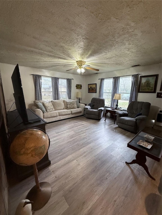 living room with ceiling fan, light wood-type flooring, plenty of natural light, and a textured ceiling