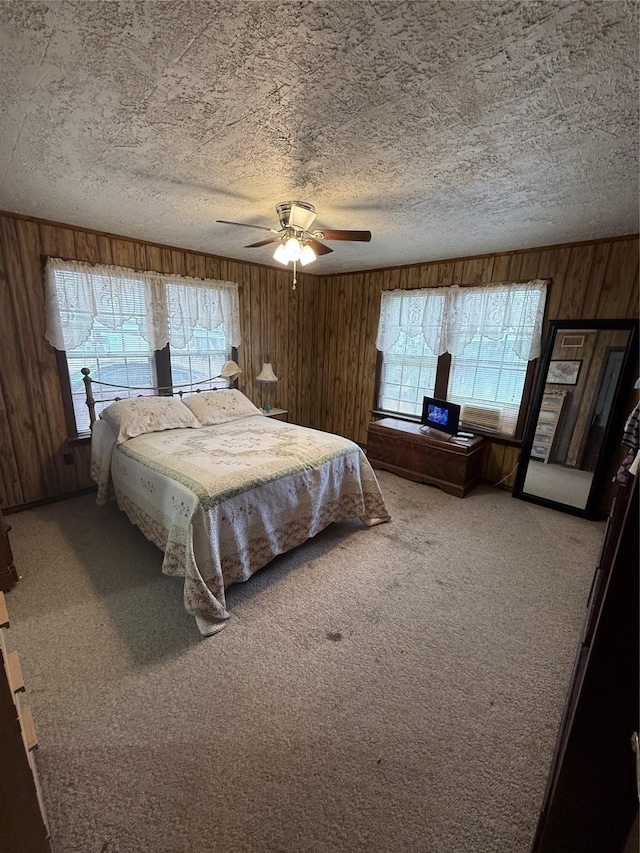 carpeted bedroom with ceiling fan, wood walls, a textured ceiling, and multiple windows