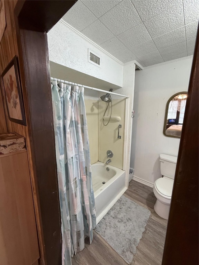 bathroom featuring wooden walls, toilet, shower / bathtub combination with curtain, and hardwood / wood-style flooring