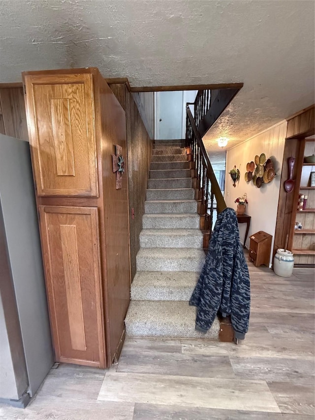 stairway featuring a textured ceiling and wood walls