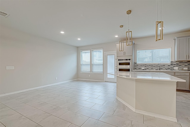 kitchen featuring backsplash, a center island, hanging light fixtures, and a healthy amount of sunlight