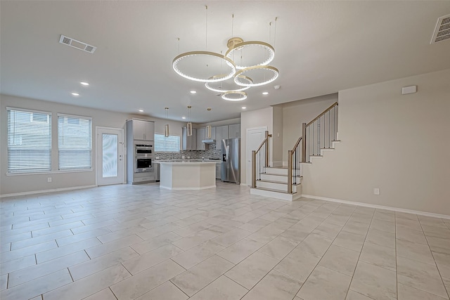 kitchen with decorative backsplash, appliances with stainless steel finishes, gray cabinetry, a kitchen island, and hanging light fixtures