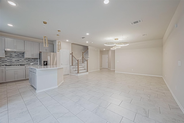 kitchen with tasteful backsplash, pendant lighting, stainless steel fridge with ice dispenser, gray cabinets, and a kitchen island