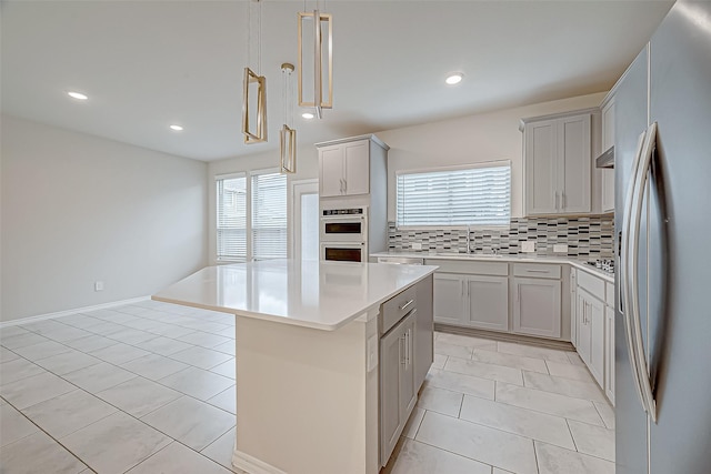 kitchen featuring a center island, stainless steel fridge, gray cabinets, tasteful backsplash, and decorative light fixtures