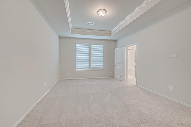 empty room with a raised ceiling, light colored carpet, and ornamental molding