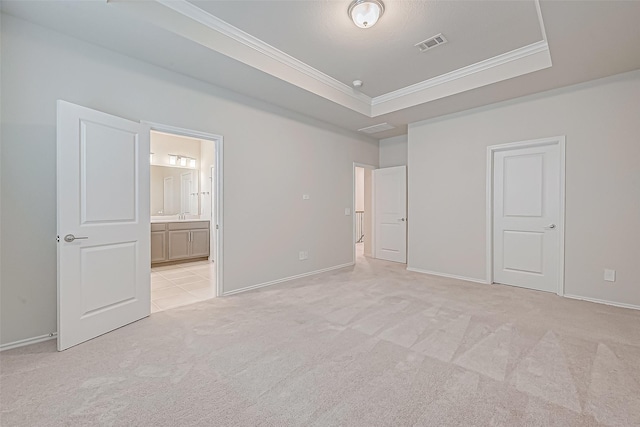 unfurnished bedroom featuring a tray ceiling, connected bathroom, light colored carpet, and ornamental molding