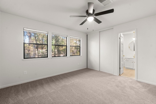 unfurnished bedroom with ensuite bathroom, a closet, ceiling fan, and light carpet