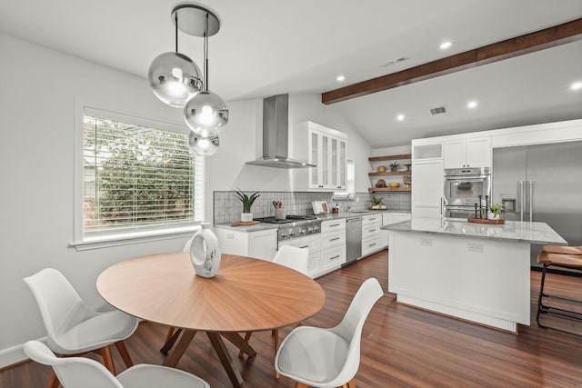 kitchen with light stone counters, wall chimney exhaust hood, stainless steel appliances, white cabinetry, and a kitchen island