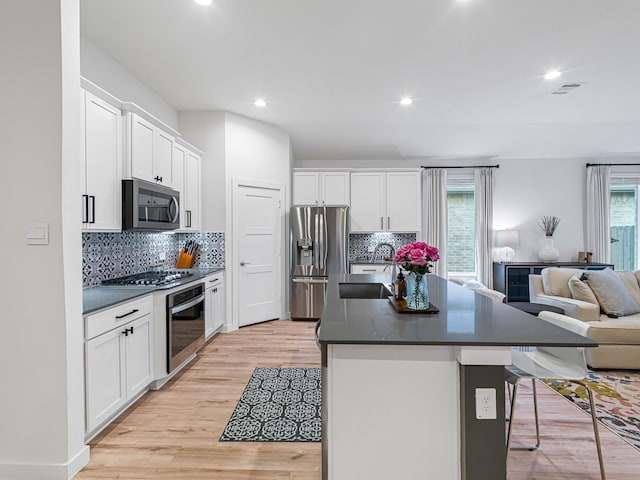 kitchen featuring sink, an island with sink, appliances with stainless steel finishes, white cabinetry, and a breakfast bar area