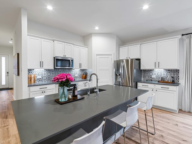 kitchen with a breakfast bar area, a kitchen island with sink, white cabinets, and stainless steel appliances