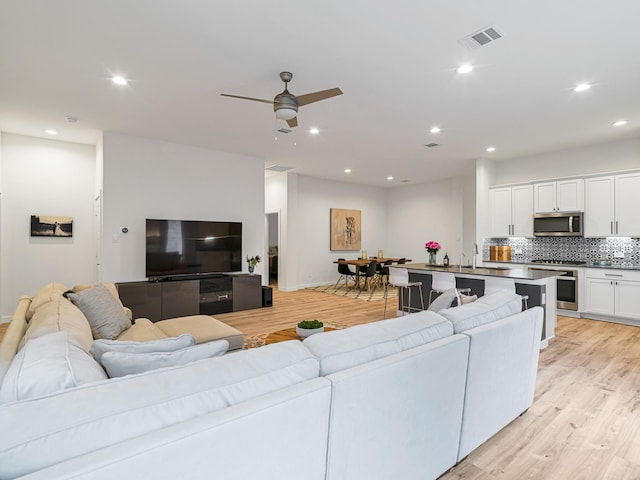 living room with ceiling fan, sink, and light wood-type flooring