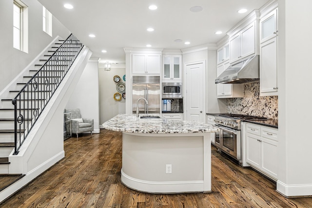 kitchen featuring built in appliances, decorative backsplash, an island with sink, and white cabinets