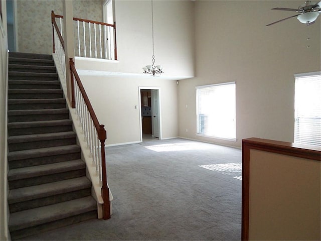 staircase featuring carpet, ceiling fan with notable chandelier, and a high ceiling