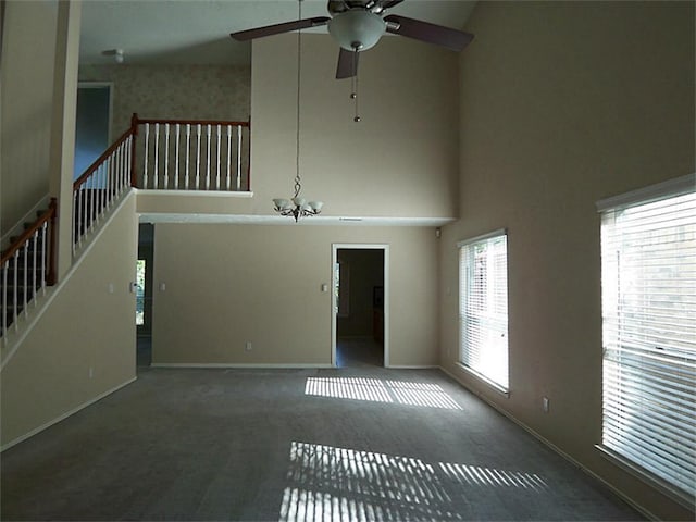 unfurnished living room with dark colored carpet, ceiling fan with notable chandelier, and high vaulted ceiling