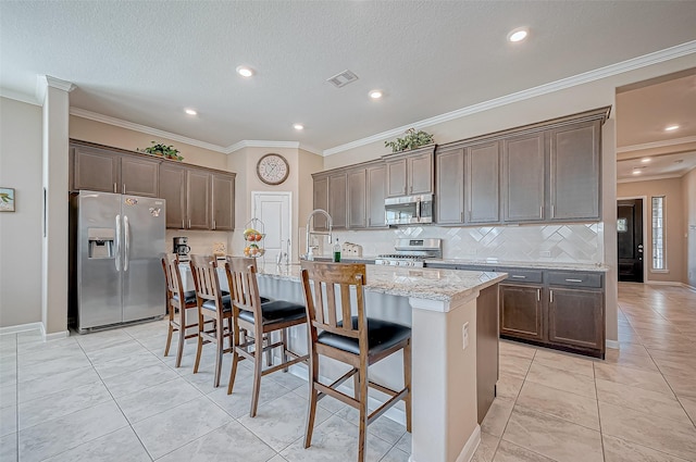 kitchen with a kitchen bar, light stone countertops, stainless steel appliances, a kitchen island with sink, and light tile patterned floors