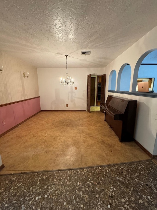 unfurnished dining area featuring a notable chandelier and a textured ceiling