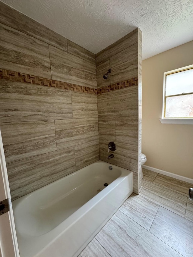 bathroom with a textured ceiling, toilet, and tiled shower / bath