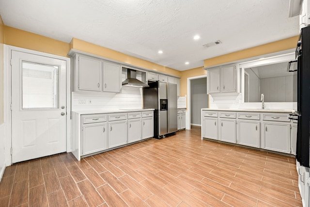 kitchen with sink, wall chimney exhaust hood, a textured ceiling, tasteful backsplash, and stainless steel fridge with ice dispenser