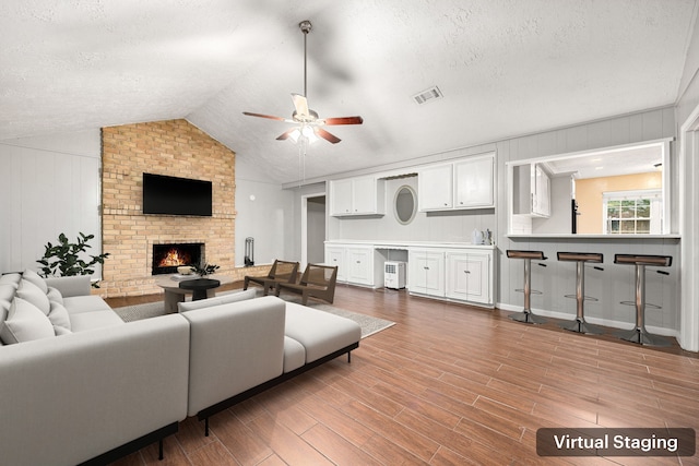 living room with a textured ceiling, ceiling fan, a fireplace, and vaulted ceiling