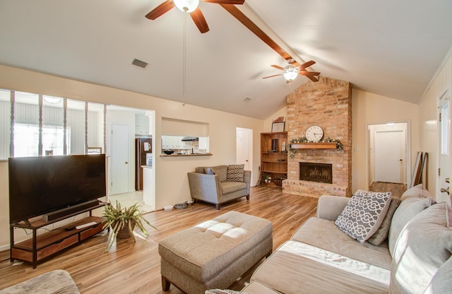 living room featuring beamed ceiling, ceiling fan, light wood-type flooring, and a fireplace