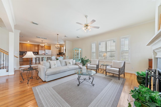 living room featuring ceiling fan with notable chandelier, light wood-type flooring, and ornamental molding