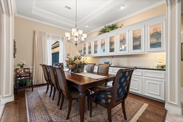 dining room with a chandelier, a tray ceiling, crown molding, and dark wood-type flooring