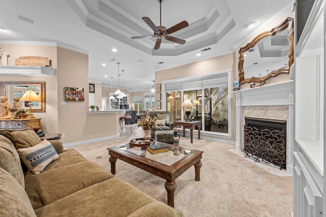 living room with ceiling fan, a raised ceiling, crown molding, light colored carpet, and a fireplace