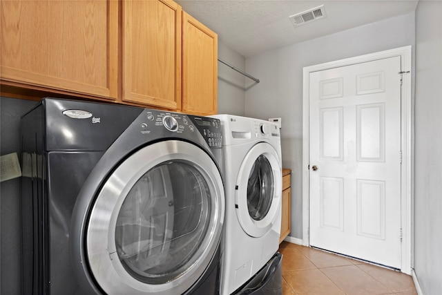 washroom with cabinets, light tile patterned floors, a textured ceiling, and washer and clothes dryer