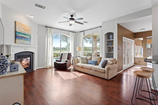 living room featuring built in shelves, ceiling fan, a tile fireplace, and dark hardwood / wood-style floors