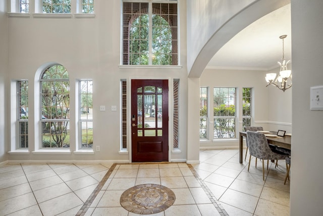 tiled foyer entrance with crown molding, a notable chandelier, and a high ceiling