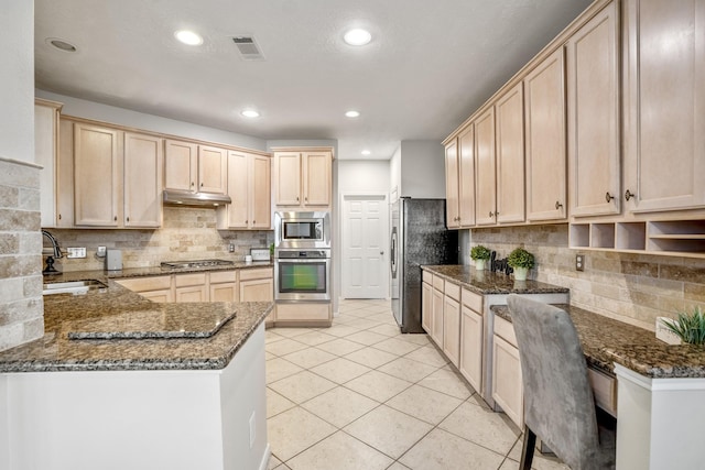 kitchen with dark stone countertops, light brown cabinets, kitchen peninsula, and appliances with stainless steel finishes