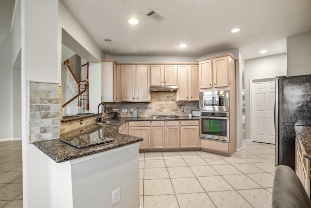 kitchen with sink, appliances with stainless steel finishes, dark stone countertops, kitchen peninsula, and light brown cabinets