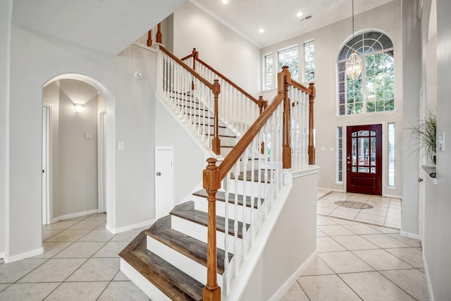 tiled entryway with crown molding and a towering ceiling