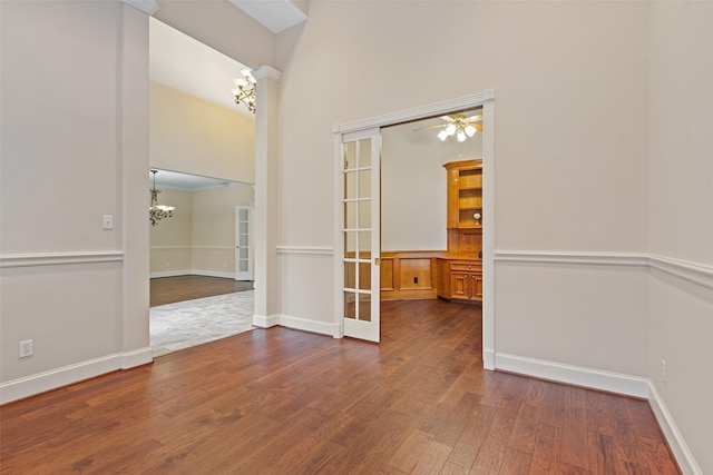 empty room with dark hardwood / wood-style flooring, ceiling fan with notable chandelier, and french doors