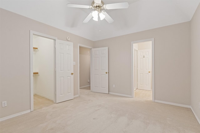 unfurnished bedroom with light carpet, a walk in closet, a closet, and ceiling fan